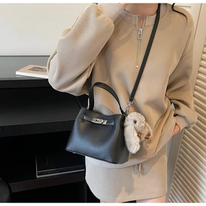 Detail of black pebbled leather bucket bag with silver turn-lock and plush bunny charm