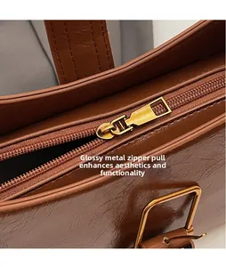 Detail view of smooth gold metal zipper pull and oil wax leather texture on brown shoulder bag