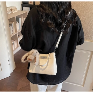 Close-up of white grainy leather bucket bag with silver clasp and plush bunny charm
