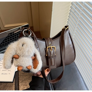 Detail of dark brown crescent bag with gold buckle and plush rabbit keychain