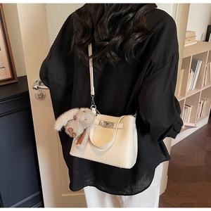 Detail of off-white lychee leather handbag with silver lock and plush bunny charm accessory