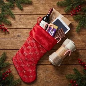 Red velvet Christmas stocking with silver bows on wood background with pine branches
