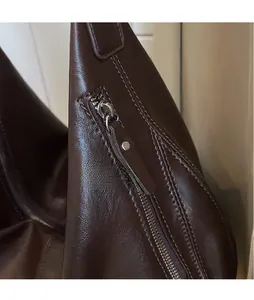 Detail of dark brown leather crescent bag featuring a long zipper pull and metal rivets