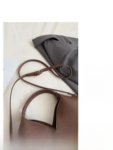 Détail d'un sac seau marron avec motif litchi et bandoulière réglable en cuir