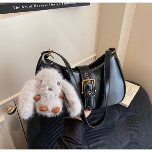 Close-up of black crossbody bag with large gold buckle and plush rabbit charm detail