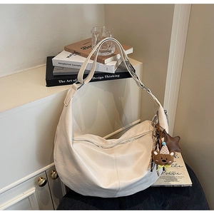 Detail of cream crescent shoulder bag with silver buckle and cute teddy bear charm