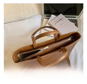 Overhead view of a large brown leather tote bag with silver zipper on a desk with laptop