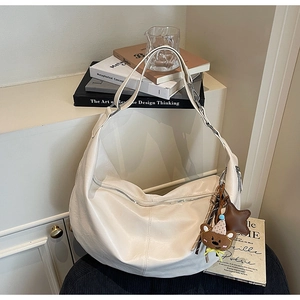 Close-up of cream half-moon hobo bag with bear charm on a stylish black stool