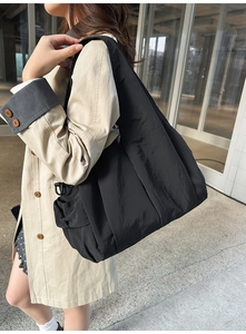 Detail view of a large black nylon tote bag with pleated texture on model