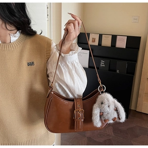 Detail of dark brown baguette bag with gold buckle and cute plush rabbit charm accessory