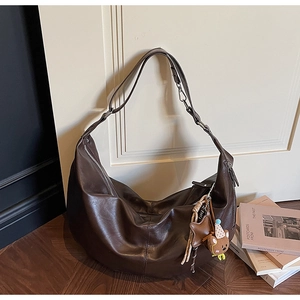 Detail of a deep brown retro hobo bag with wide shoulder strap and cute bear charm pendant