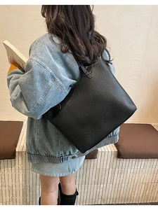 Detail of a large black pebbled leather tote bag worn by a model in a cozy indoor setting