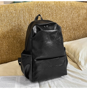 Detail of a black PU leather backpack with a front zipper pocket on a white bed