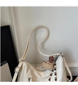 Détail du sac en cuir crème avec charm ours en peluche et chaîne à perles