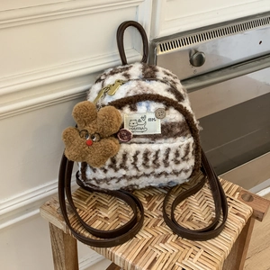 Detail of plush mini backpack featuring heart patterns and cute brown flower pendant