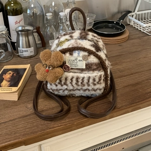 Detail of plush mini backpack with bear charm and vintage brand label on wood table