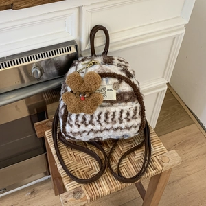 Detail of plush striped backpack with bear charm and leather straps on wooden stool