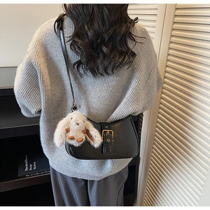 Detail of black crescent shoulder bag with glossy leather and cute plush bunny charm