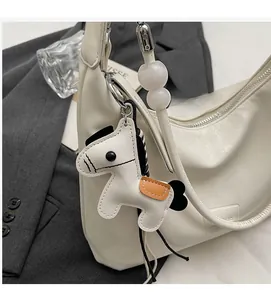 Gros plan d'un sac demi-lune blanc avec breloque cheval en cuir sur un blazer gris