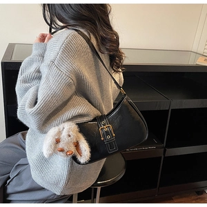 Detail of black glossy patent leather shoulder bag with gold buckle and plush rabbit charm