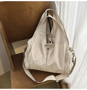Detail of beige nylon tote bag on a wooden chair showing its wrinkled texture and side pocket