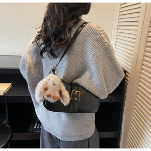 Detail of black leather shoulder bag with vintage gold buckle and plush rabbit charm
