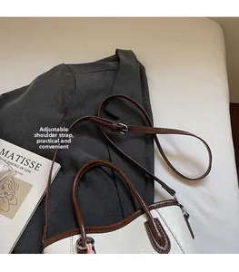 Close-up of cream bucket bag with brown trim and adjustable strap on neutral background