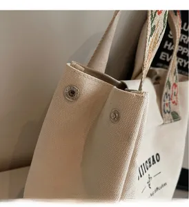 Detail of silver snap button and floral embroidered strap on off-white canvas tote bag