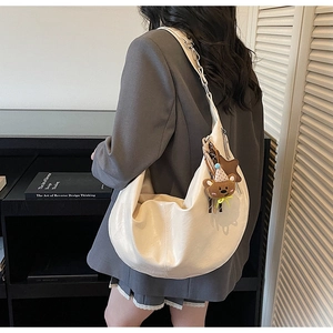 Cream hobo bag featured with a brown teddy bear charm and elegant matte leather finish