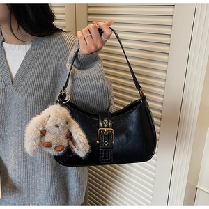 Detail of black semi-moon hobo bag with gold buckle and white plush bunny charm