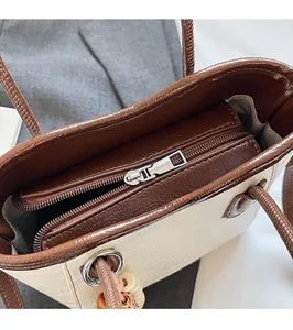 Detail of silver metal zipper closure on cream and brown faux leather bucket bag