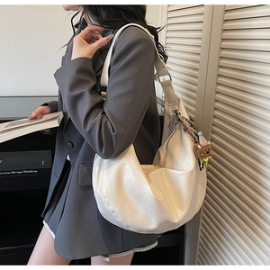 Detail of cream half-moon tote bag with brown bear pendant worn by model in gray blazer