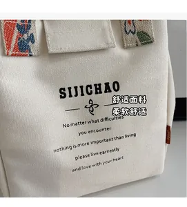 Macro detail of canvas bucket bag showing black lettering and colorful floral handle strap