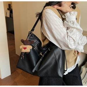 Close-up of black lychee texture tote bag with a cute bear pendant and golden metal hardware
