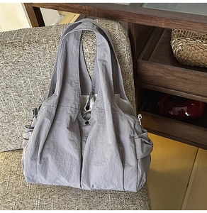 Detail view of a gray nylon tote bag on a textured chair showing side pockets and snap button