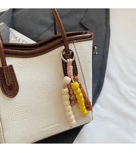 Close-up of beige lychee texture bucket bag with brown trim and beaded metal charm