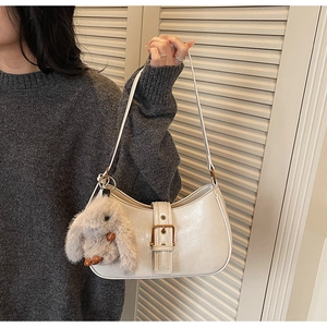 Detail of a beige crescent hobo bag with gold buckle and plush rabbit charm