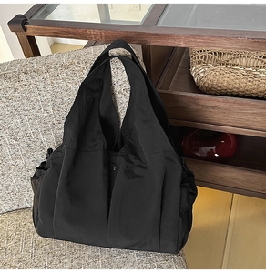 Detail of black nylon tote bag with matte texture and metallic snap closure on sofa