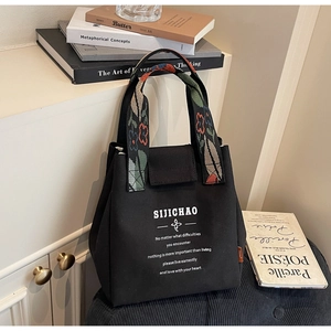 Detail of black canvas bucket bag featuring floral embroidery strap and inspirational text