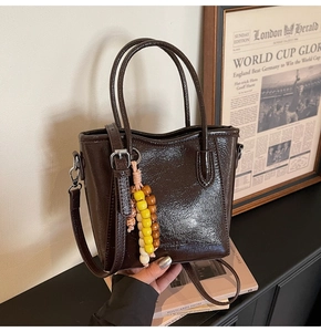 Close-up of a dark brown bucket bag featuring a glossy finish and colorful beaded charm