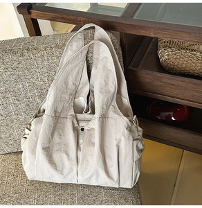 Close-up of beige nylon tote bag showing textured fabric, wide strap and side pockets