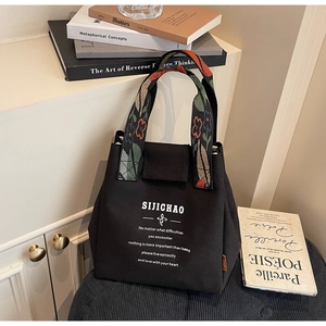 Detail of black canvas bucket bag featuring floral embroidered handles and text print