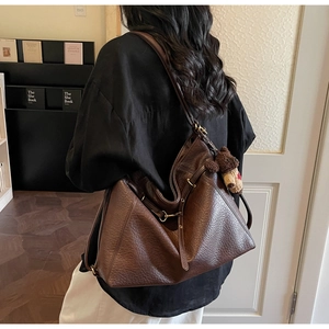 Brown leather tote bag with gold buckle and cute bear charm shown in a cozy home setting