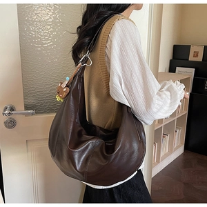 Detail of dark brown crescent shoulder bag with silver buckle and bear charm on strap