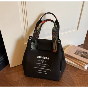 Detail of black canvas bucket bag featuring floral jacquard handle and printed text