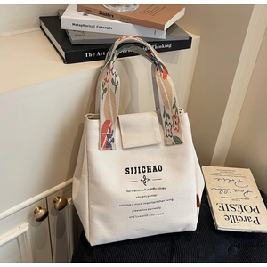 Detail of canvas tote bag with floral embroidered handles and minimalist printed text