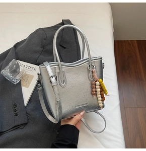Detail of silver tote bag featuring metallic pleated texture and colorful wooden bead charm
