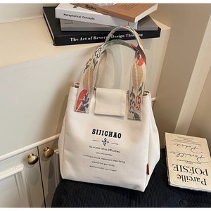 Detail of cream canvas tote bag featuring floral embroidered handle and magnetic closure
