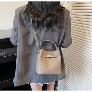Detail view of taupe lychee leather bucket bag with metal turn-lock on a model in a suit