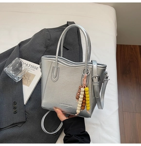 Detail of silver metallic textured bucket bag with boho wooden bead tassel and top handle
